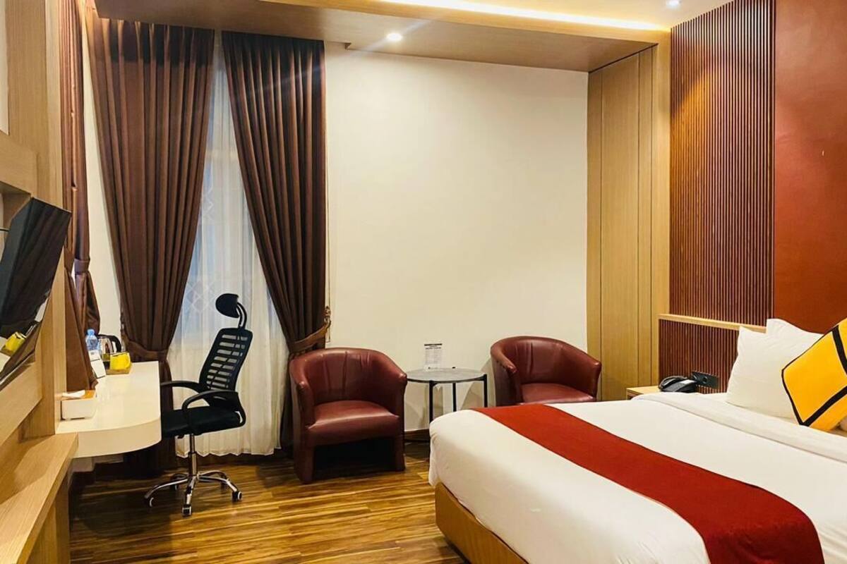 A hotel room with a bed, desk, two chairs, a small table, and a TV.