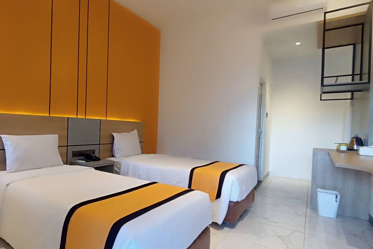 A hotel room with two beds, a nightstand, a small table, and a bathroom visible through an open door.