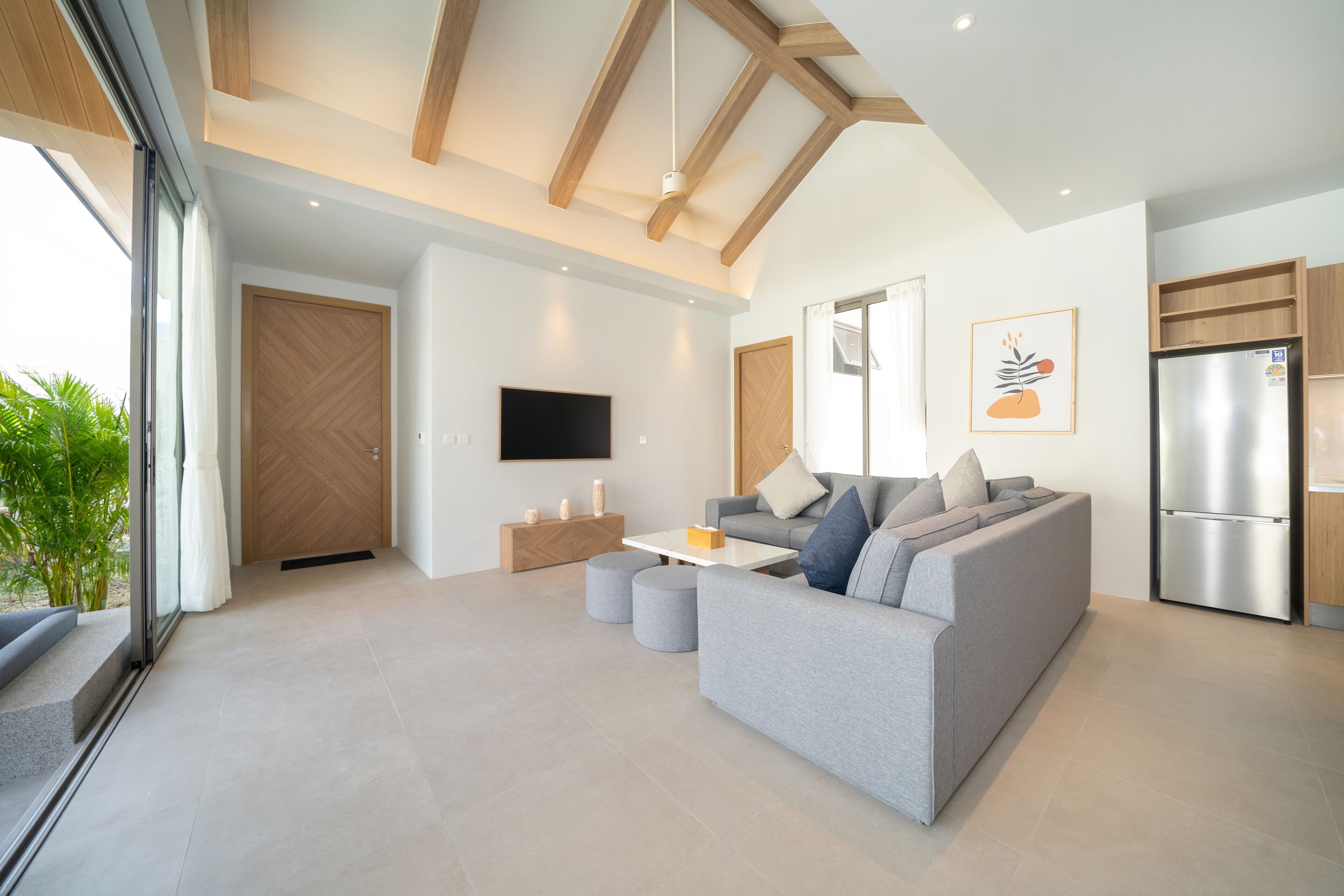 A modern living room with a grey sofa, a flat-screen TV, and a wooden ceiling.