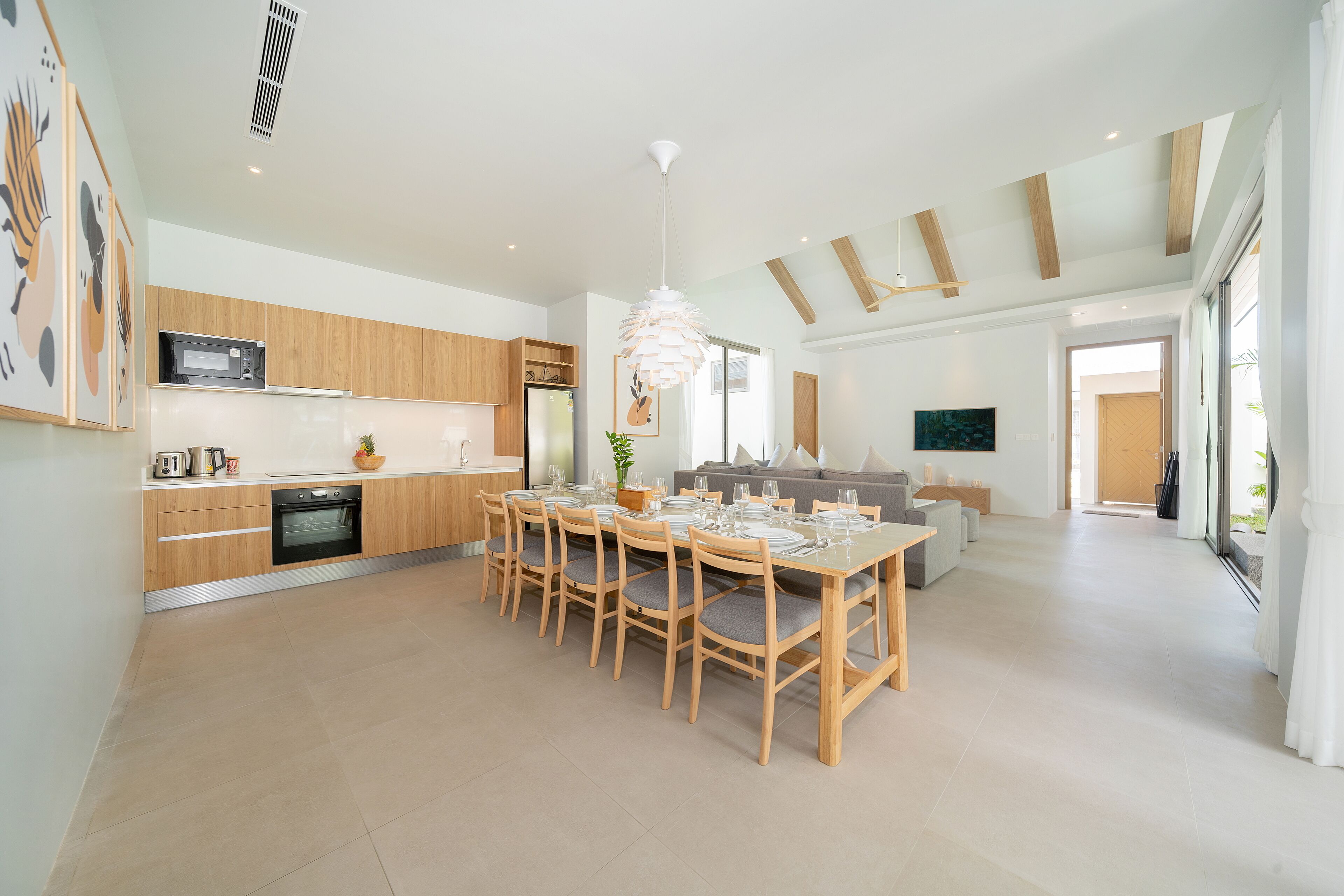 A modern kitchen with wooden cabinets, a dining area with a large table and chairs, and a living area with a sofa and a TV.