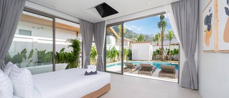 A modern bedroom with a large bed, a view of a swimming pool, and a balcony with plants.