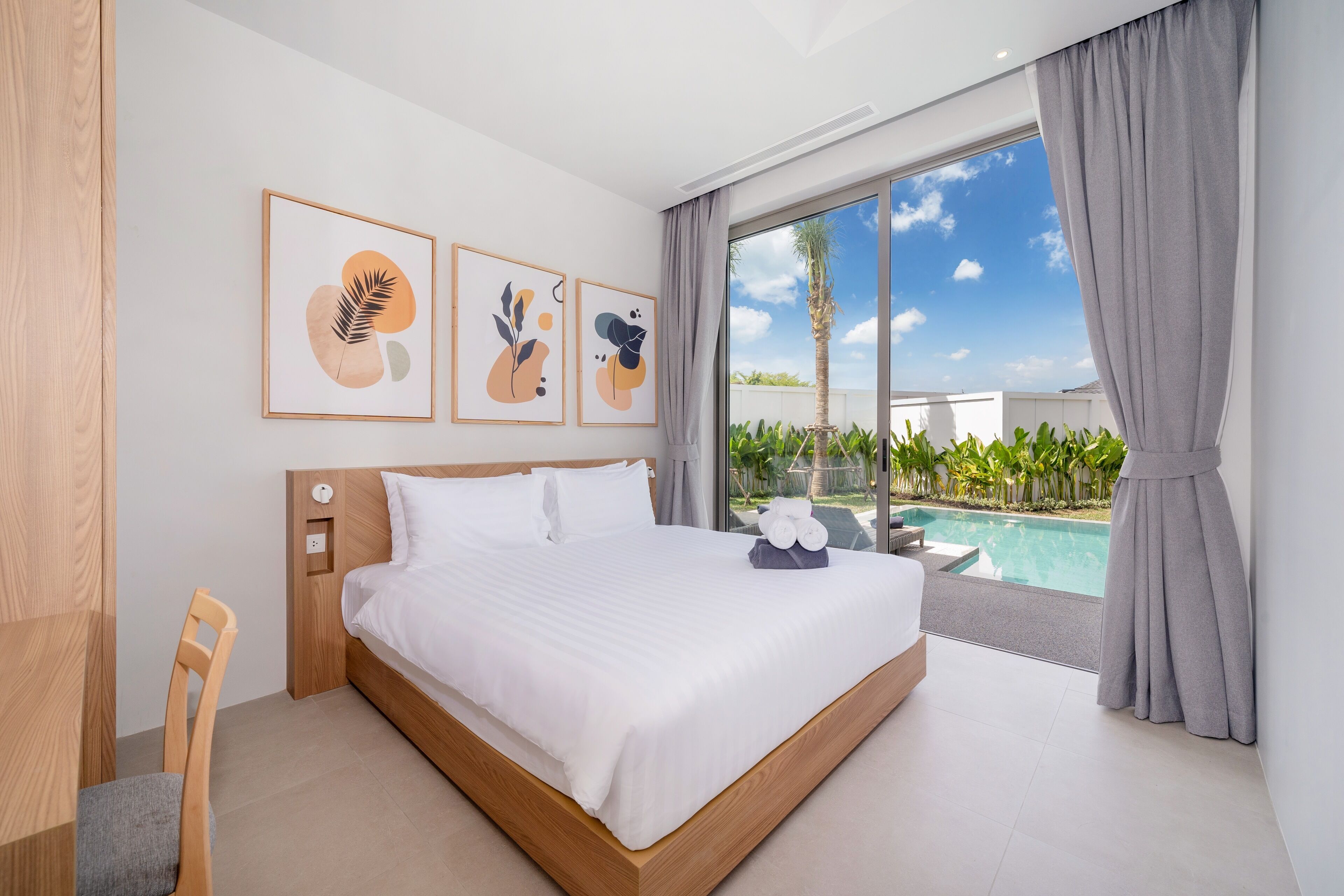 Une chambre d’hôtel moderne avec un grand lit, une tête de lit en bois, une vue sur une piscine et des œuvres d’art accrochées au mur.