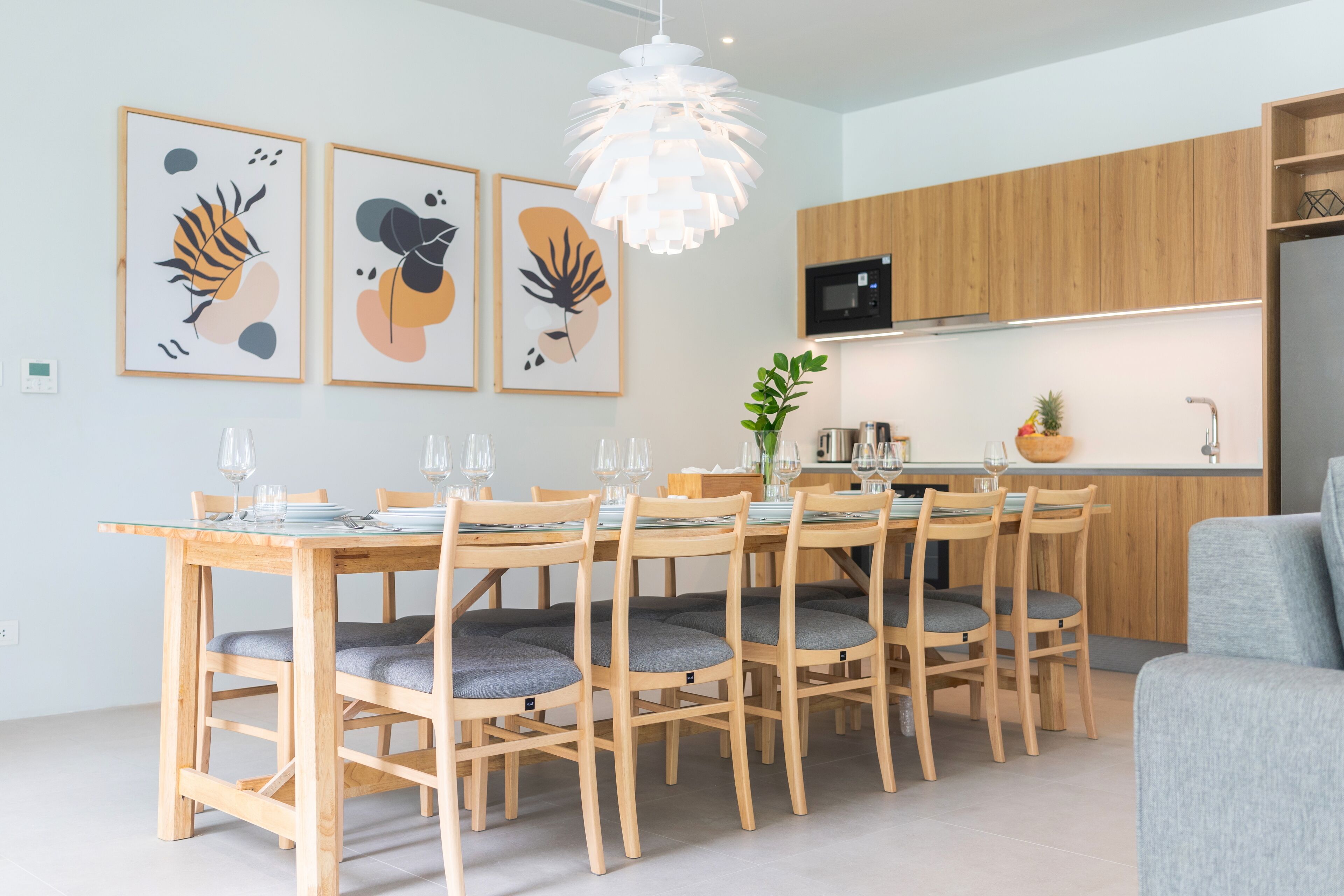 A modern kitchen with wooden cabinets, a dining table with chairs, and framed artwork on the wall.