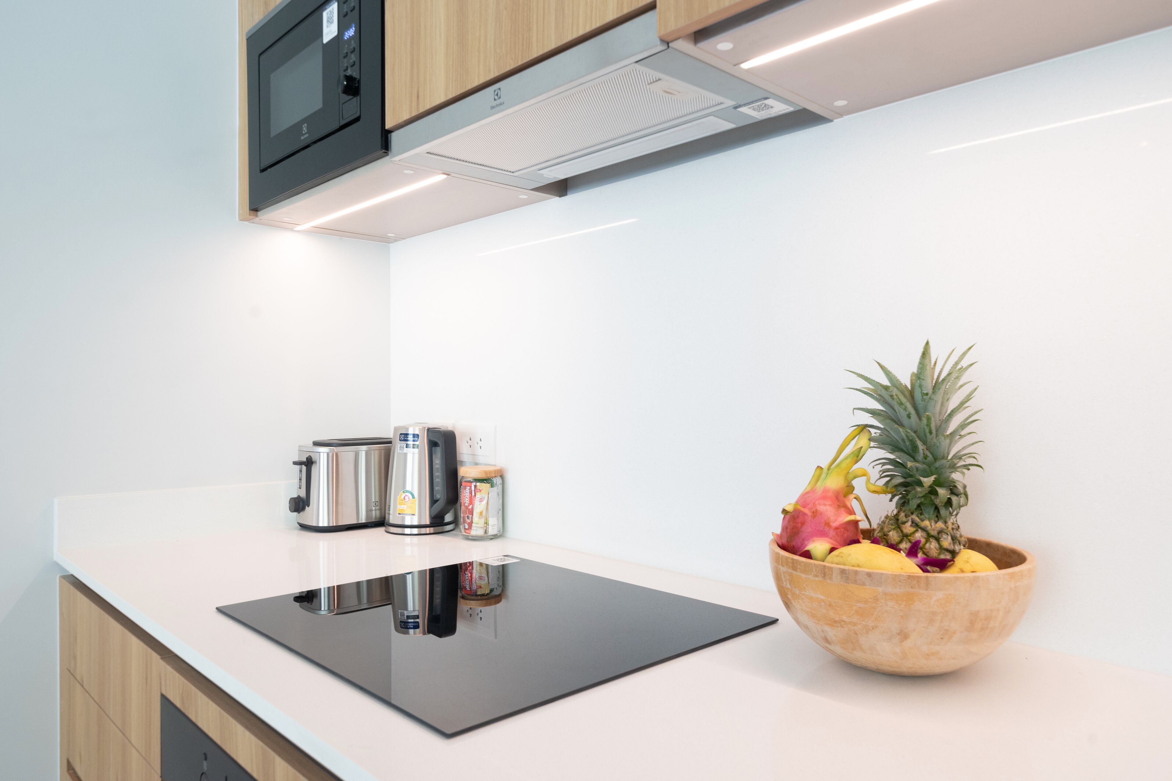 A modern kitchen with a black induction cooktop, stainless steel appliances, and a wooden bowl of fruit on the counter.