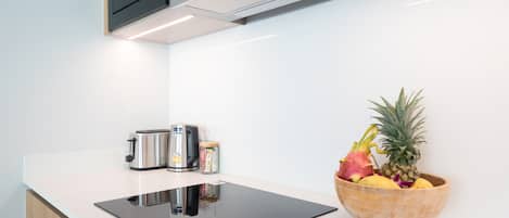 A modern kitchen with a black induction cooktop, stainless steel appliances, and a wooden bowl of fruit on the counter.