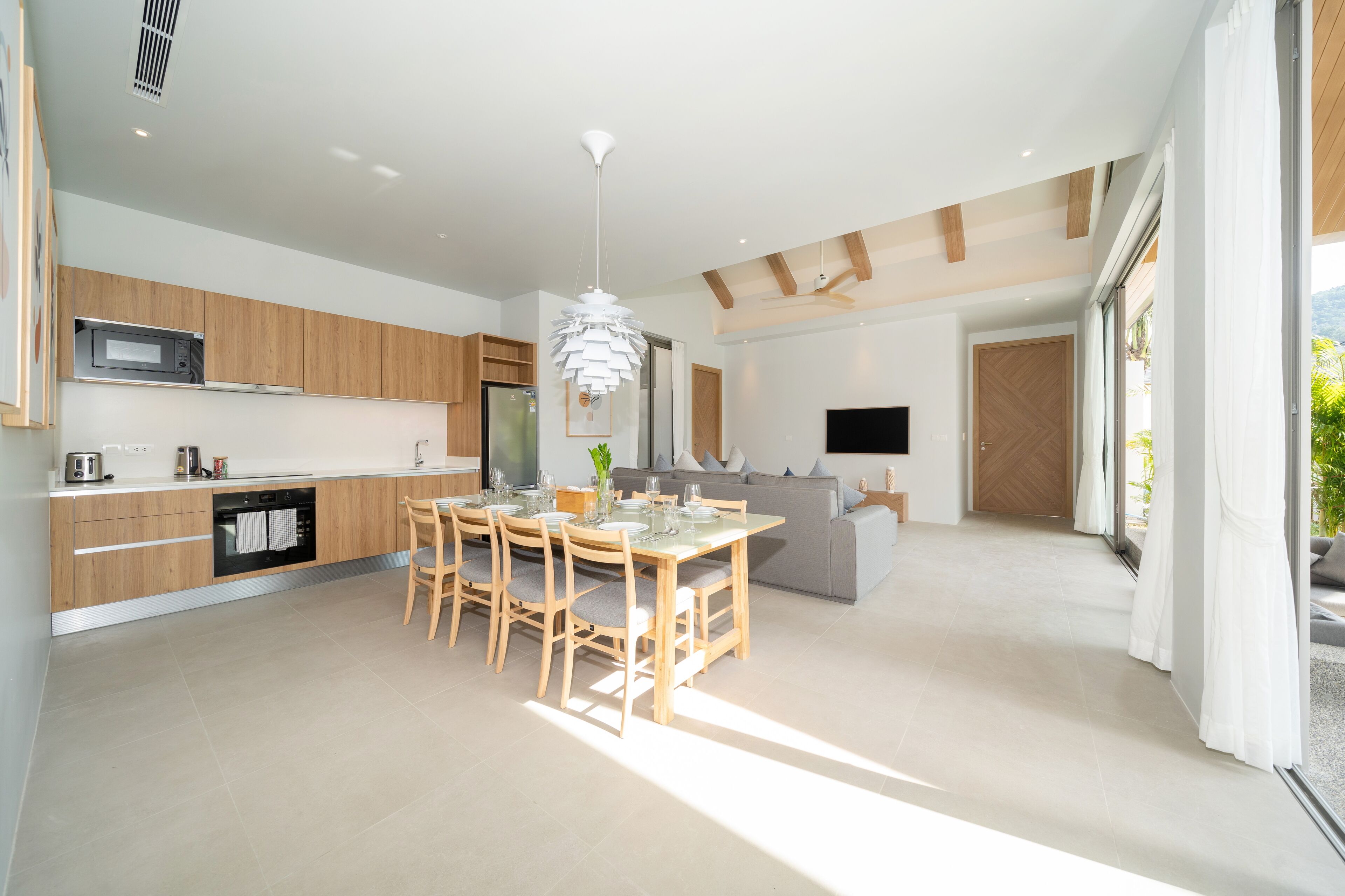 Een moderne keuken met houten kastjes, een eethoek met een tafel en stoelen, en een groot raam dat zorgt voor natuurlijk licht.