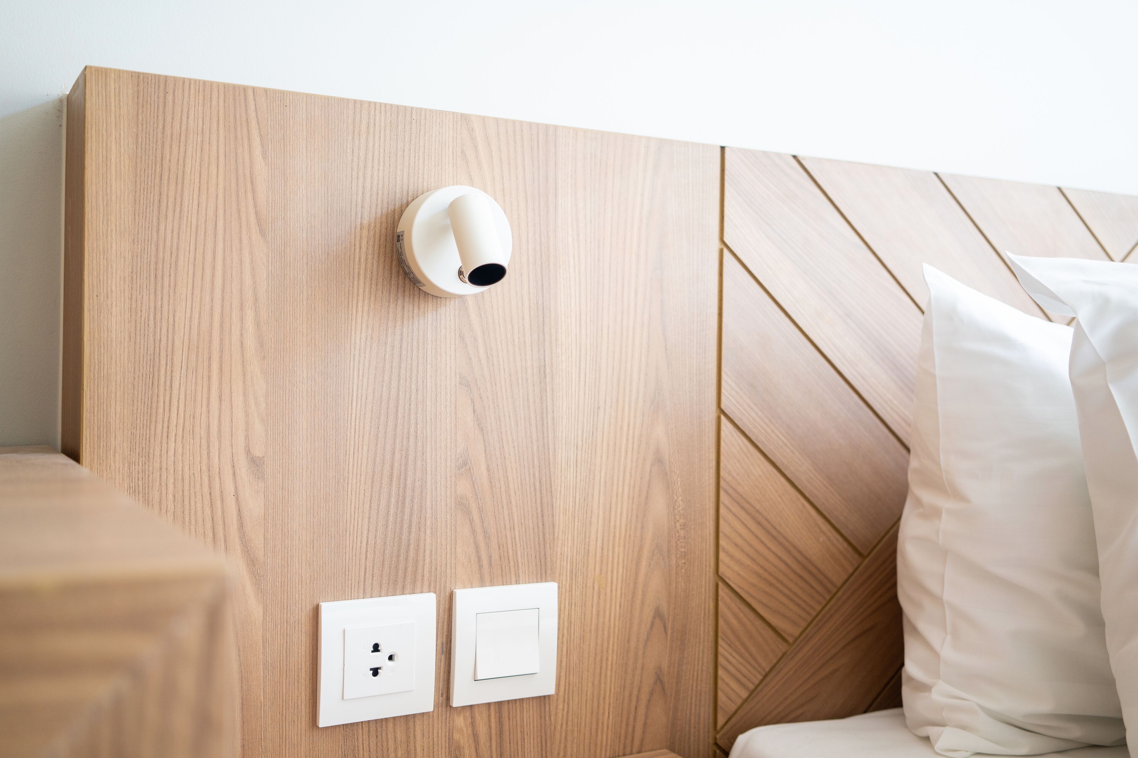 Una testiera in legno con altoparlante integrato e due interruttori della luce fissati al muro.
