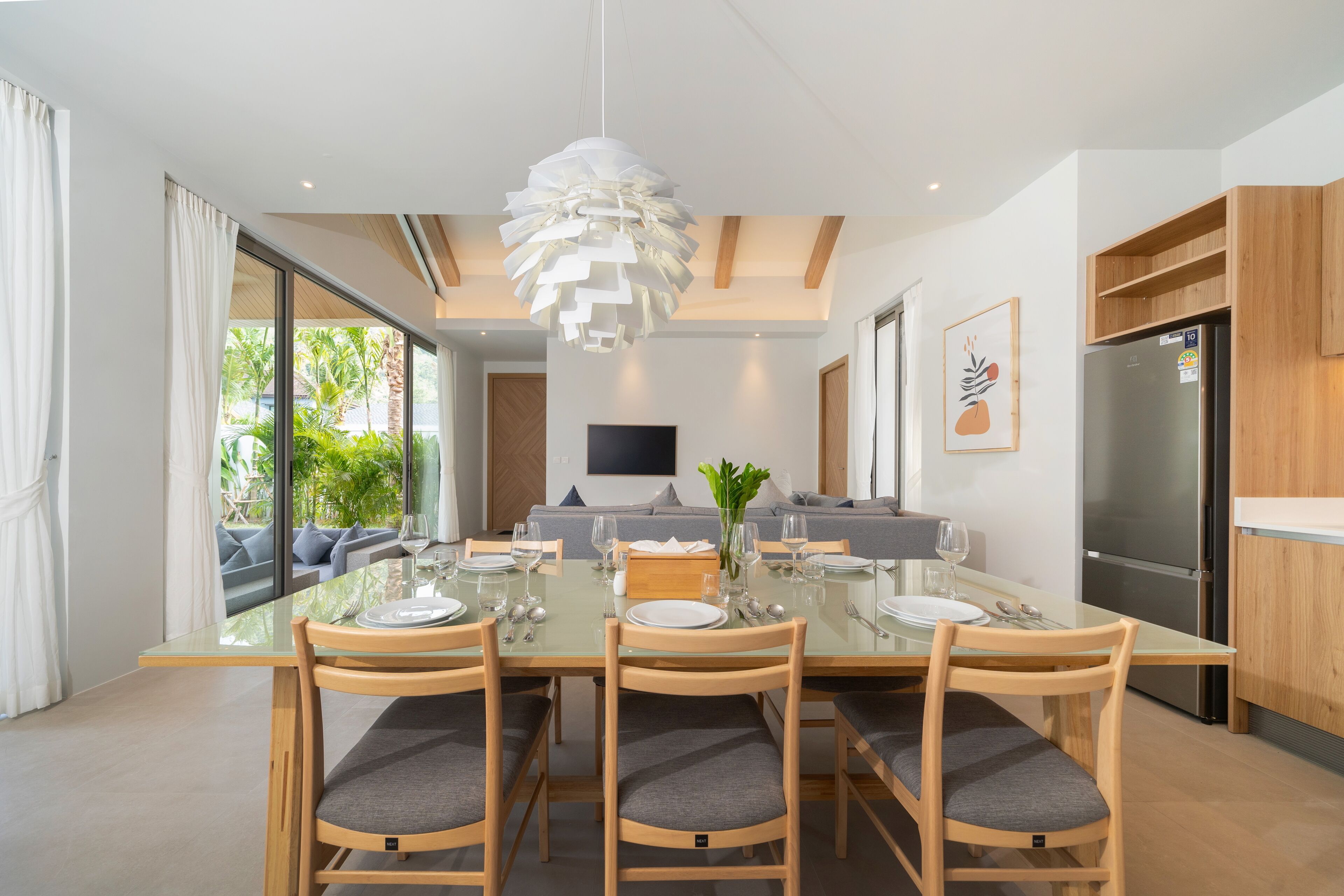 A modern dining area with a glass table, wooden chairs, and a central light fixture.