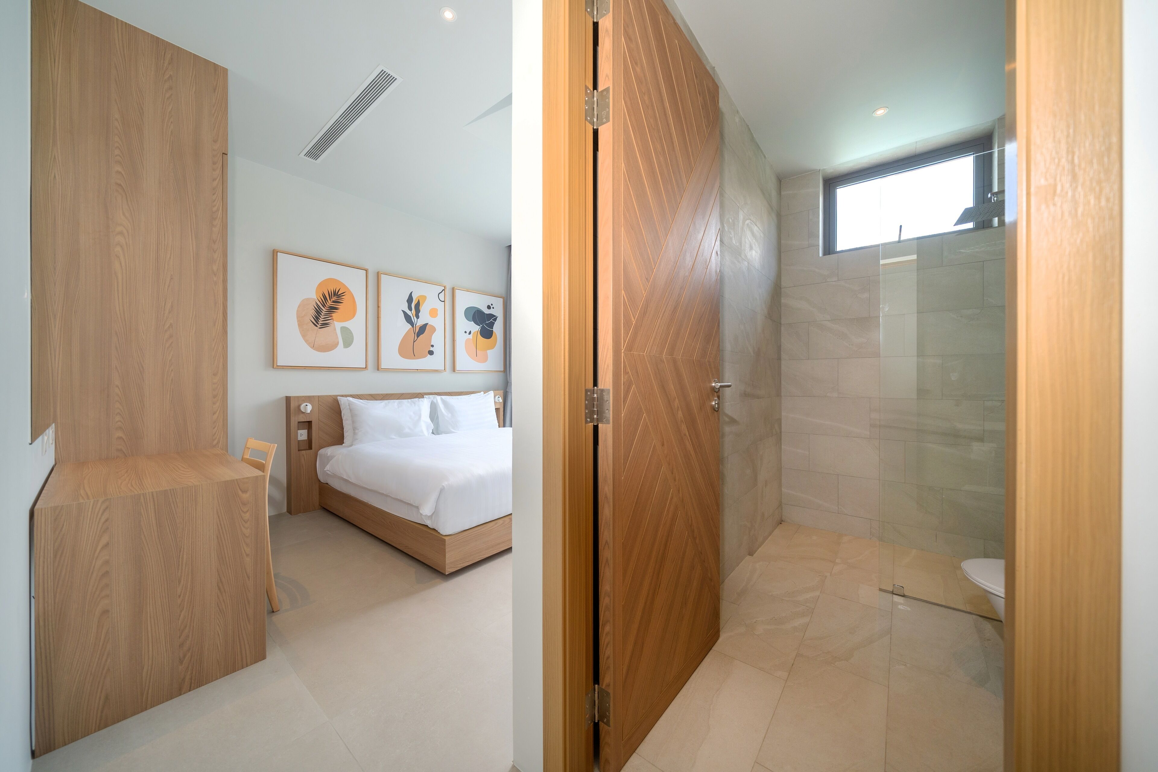 Una habitación de hotel moderna con un armario de madera, una cama con ropa de cama blanca y un área de ducha con puerta de cristal.