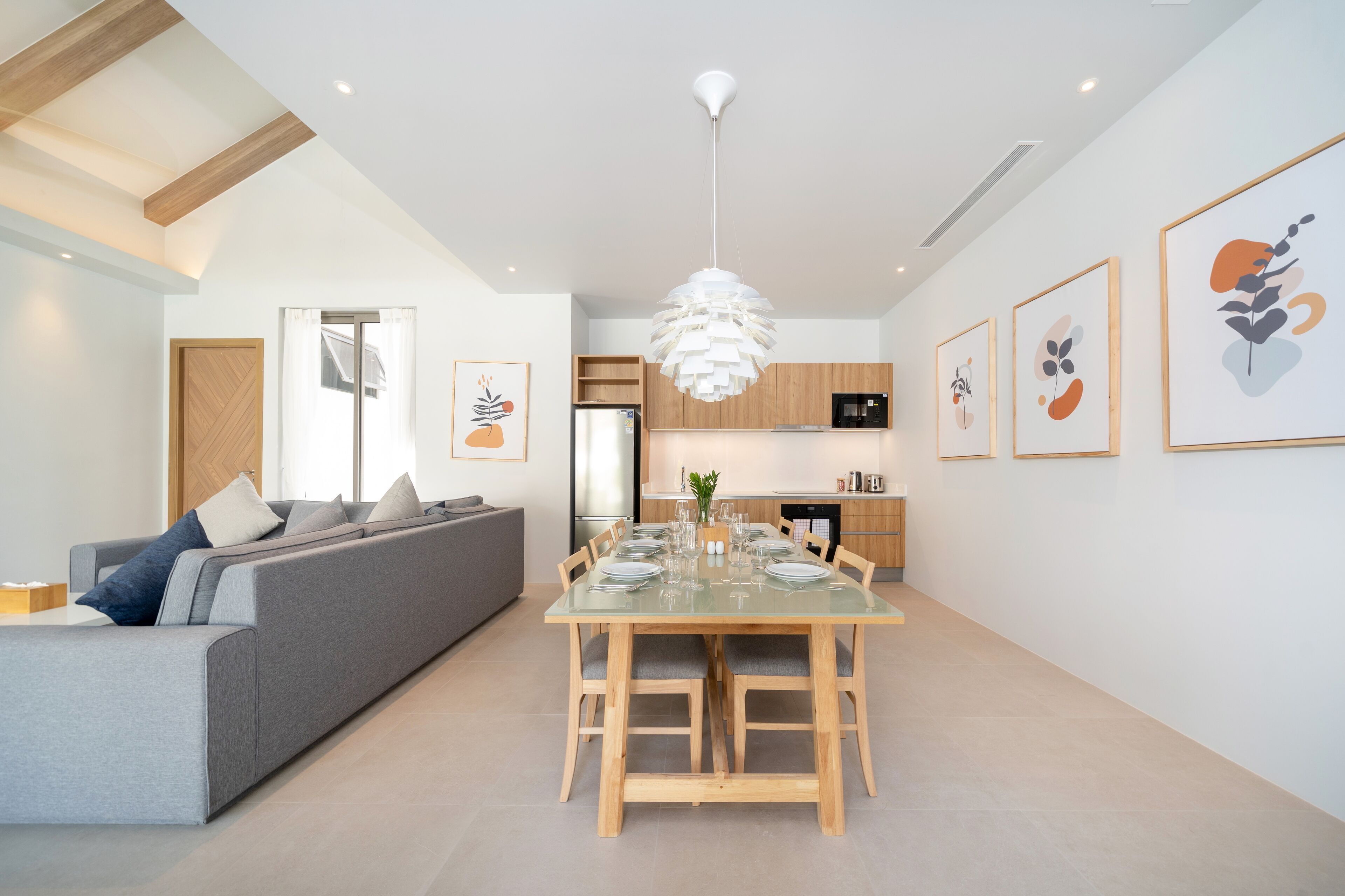 A modern living room with a grey sofa, wooden dining table, and a kitchen in the background.