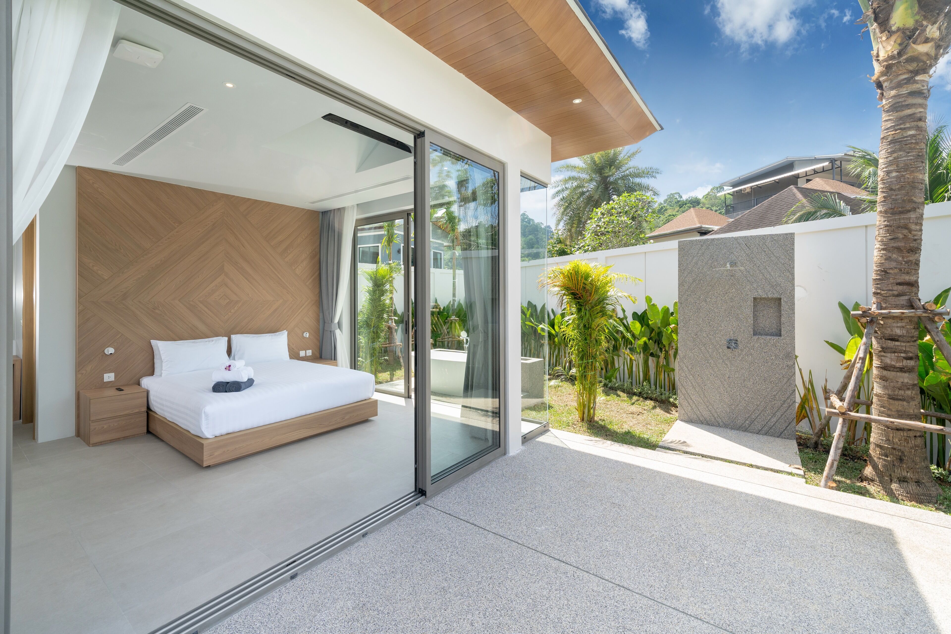 Une chambre moderne avec un grand lit, des portes-fenêtres coulissantes donnant sur un balcon et une vue sur un jardin luxuriant.