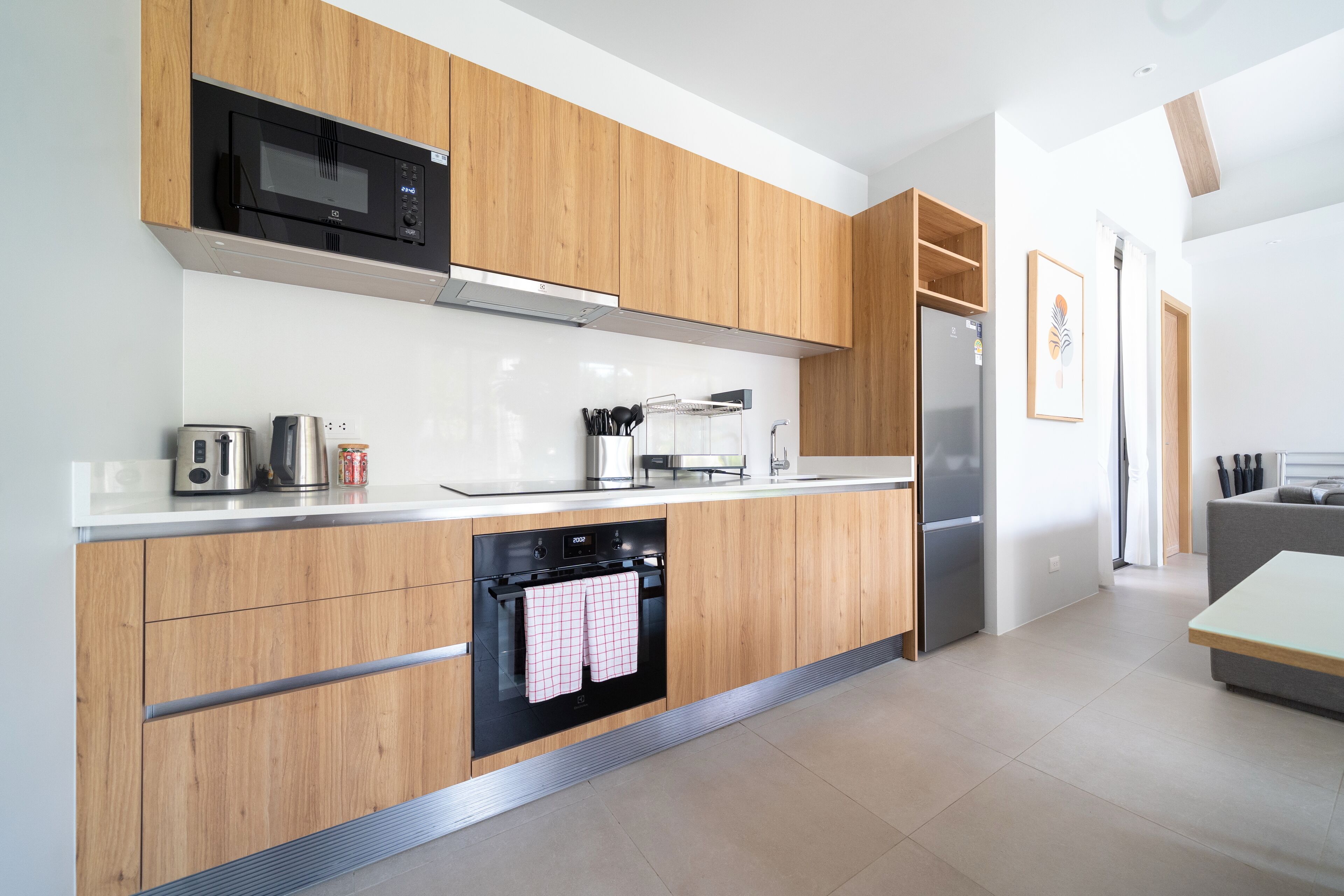 A modern kitchen with wooden cabinets, a microwave, a toaster, a kettle, and a refrigerator.