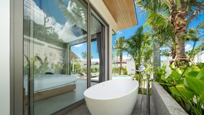 A modern bathroom with a freestanding bathtub, large windows, and a view of a pool and palm trees. - Himmapana Villas - Grand Valley (Kamala)