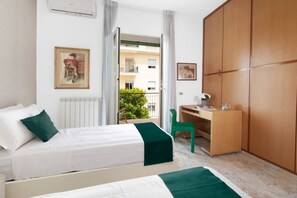 Habitación de hotel con cama, escritorio, armario y balcón con vistas a edificios y vegetación.