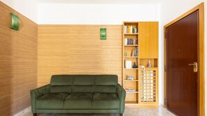 Un sofá verde en una habitación con paneles de madera, una estantería y una puerta de madera.