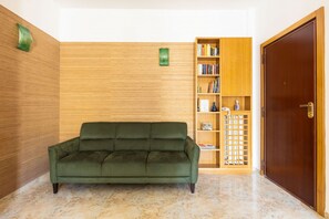 Ein grünes Sofa in einem Raum mit Holzvertäfelung, einem Bücherregal und einer Holztür.