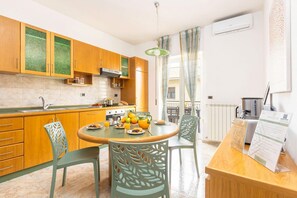 A modern kitchen with wooden cabinets, a round dining table, and chairs. There is a fruit bowl on the table, and a coffee machine on the counter.