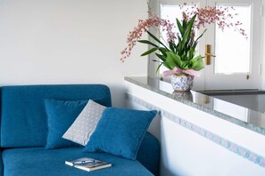 Un canapé bleu avec un livre et des lunettes, un vase avec des fleurs roses et, au fond, une porte blanche.
