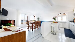 A modern kitchen with white cabinetry, a dining area with wooden chairs, and a view through large windows. - Sea view Rooftop Apartment with Jacuzzi & Garden (Sorrento)