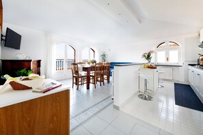 Une cuisine moderne avec des meubles blancs, un coin repas avec des chaises en bois et une vue dégagée grâce à de grandes fenêtres.