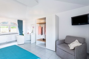 A modern room with a grey sofa, a TV mounted on the wall, and a window with curtains. - Sea view Rooftop Apartment with Jacuzzi & Garden (Sorrento)