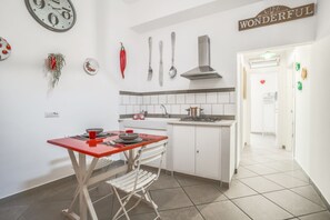 Een keuken met witte kastjes, een rode tafel en een witte stoel. Er zijn decoraties aan de muur, waaronder een klok, een rode peper en keukengerei. Een bord op de muur zegt: "LIFE IS WONDERFUL".