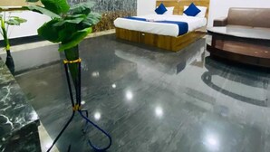 Una habitación de hotel con cama, sofá, una planta grande en maceta y suelo de mármol.