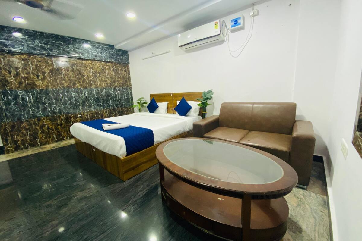 Een hotelkamer met een bed, een bruine leren bank, een glazen salontafel en een airconditioning aan de muur.