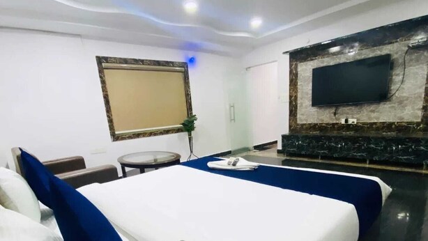 Habitación de hotel con una cama grande, un televisor de pantalla plana montado en la pared, una mesita redonda y una planta en maceta.