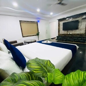 A hotel room with a large bed, a flat-screen TV mounted on the wall, a small round table, and a potted plant. - Hotel Kp Suites Grand (Hyderabad)