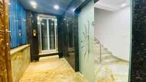 Un pasillo con suelo de mármol, una puerta de cristal, una pared azul y una escalera.
