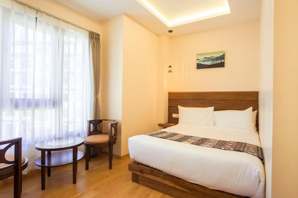 A hotel room with a bed, a chair, a small table, and a painting on the wall.