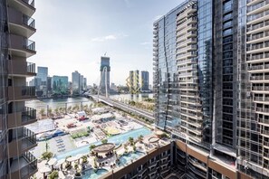 A high-rise building with a rooftop pool area, including lounge chairs and umbrellas, overlooking a river with a bridge in the background. - BeVista Metropole Thu Thiem (Ho Chi Minh City)