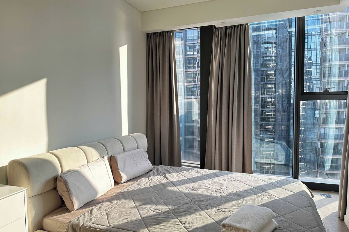 Una camera da letto moderna con un letto grande, un divano e vista sulla città attraverso ampie finestre.