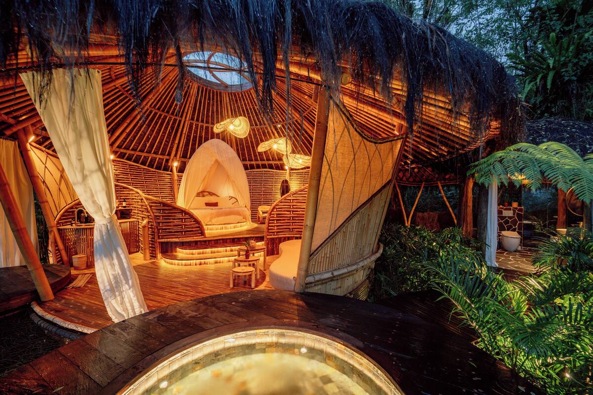 Una estructura con techo de paja, interior circular, jacuzzi y terraza de madera.