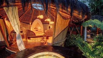 A thatched-roof structure with a circular interior, a hot tub, and a wooden deck.