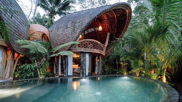 Una località turistica con una grande piscina, una zona salotto esterna coperta e una rigogliosa vegetazione tropicale.