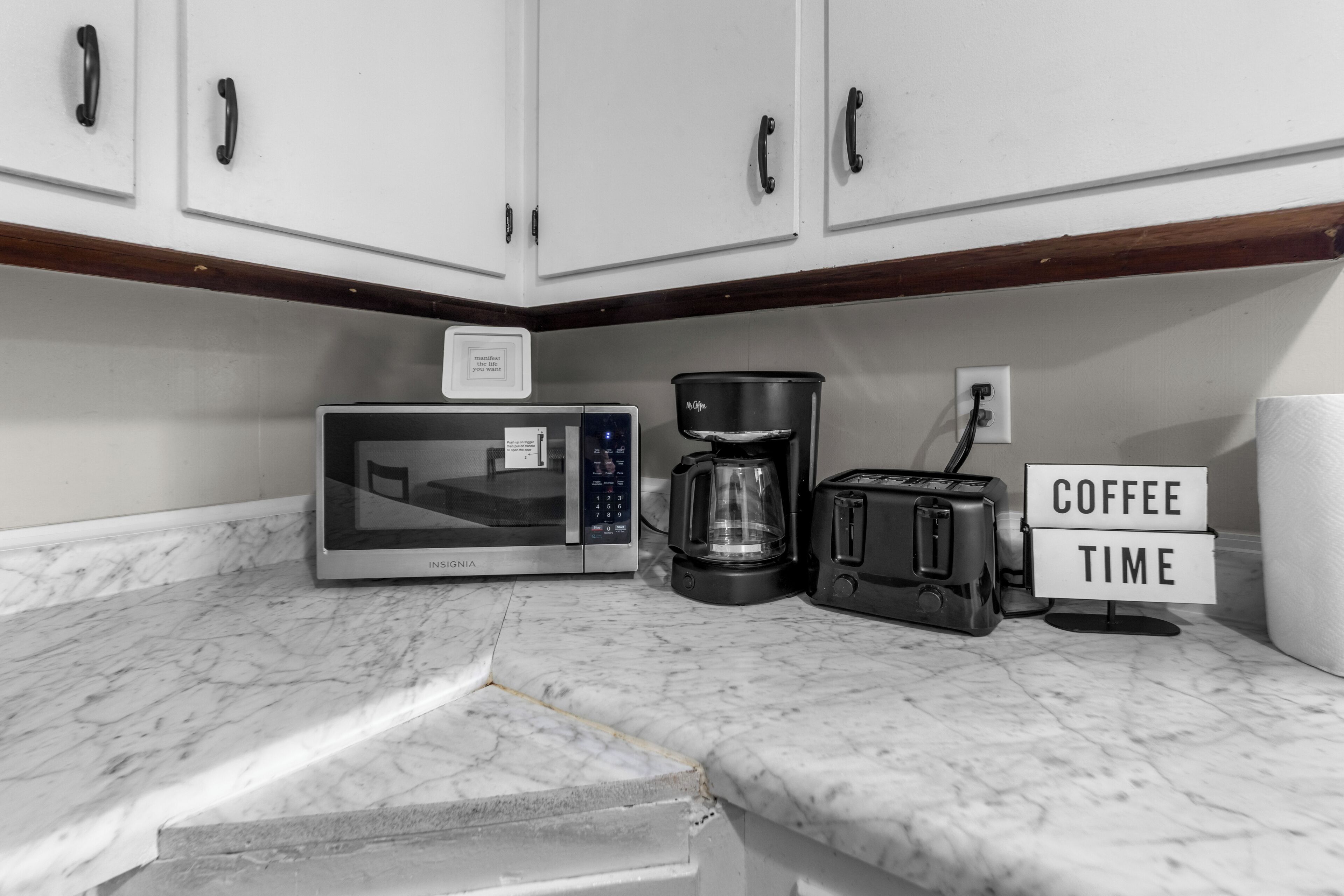 A kitchen with a microwave, coffee maker, and toaster on a marble countertop.