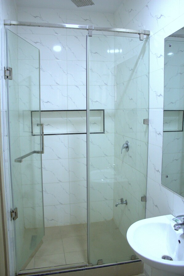 A glass-enclosed shower with a white marble wall and a white sink with a mirror.