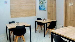 A conference room with four tables and chairs, a wooden panel on the wall, a painting, and a door with a 'Restricted Area' sign. - Caritas Inn Ilasan (Lekki)