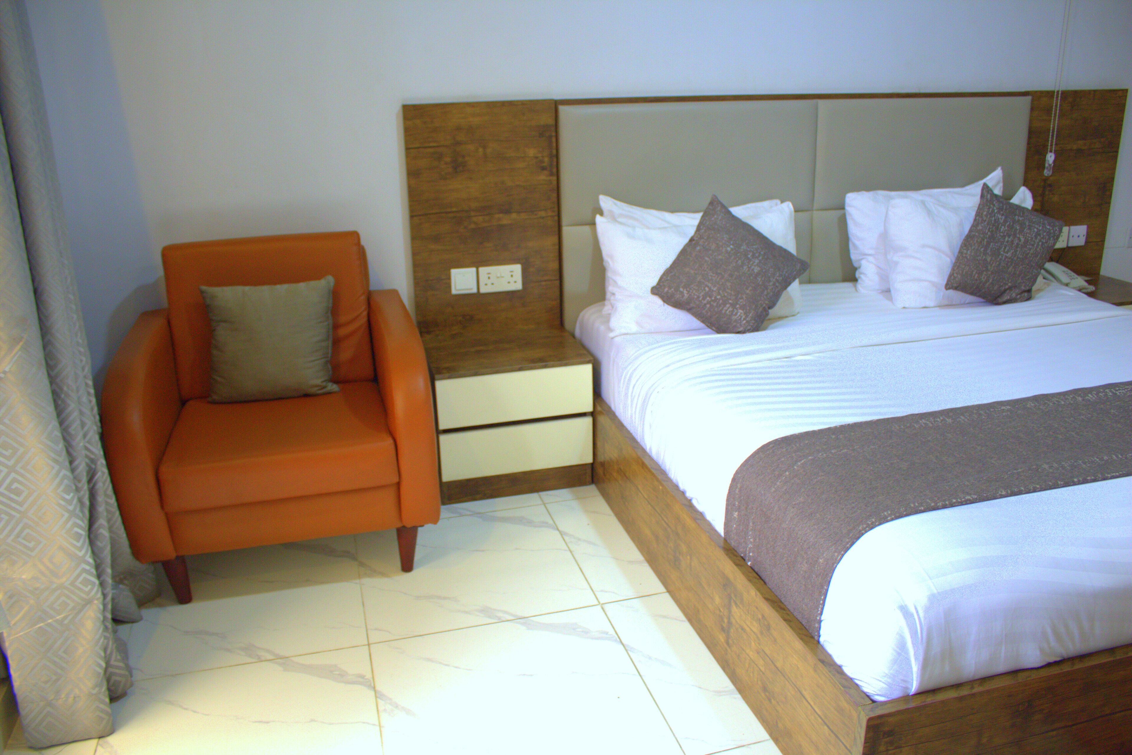 A hotel room with a bed, an orange armchair, and a nightstand.