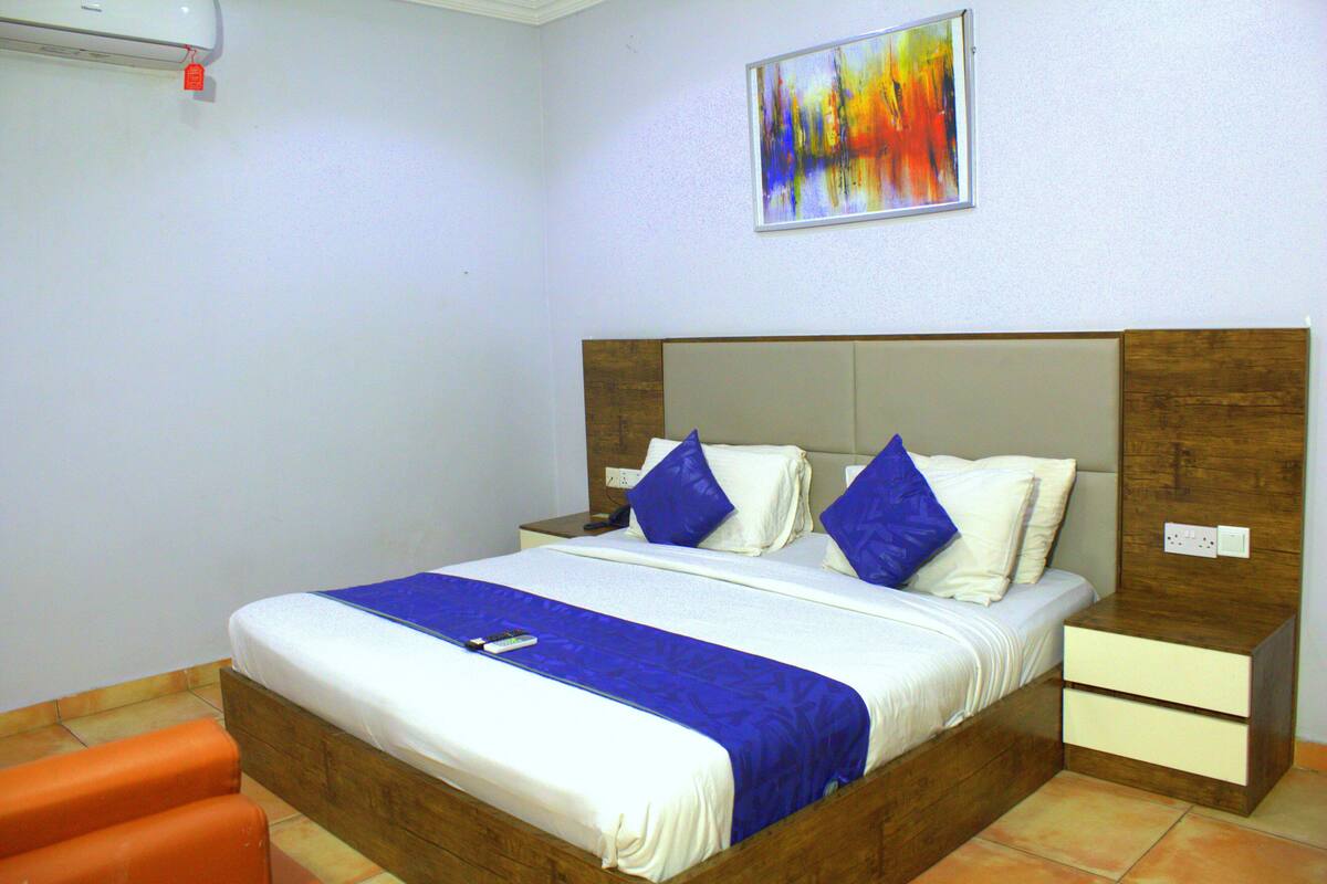 Una cama doble con cabecera de madera, dos mesitas de noche y una colcha azul y blanca.