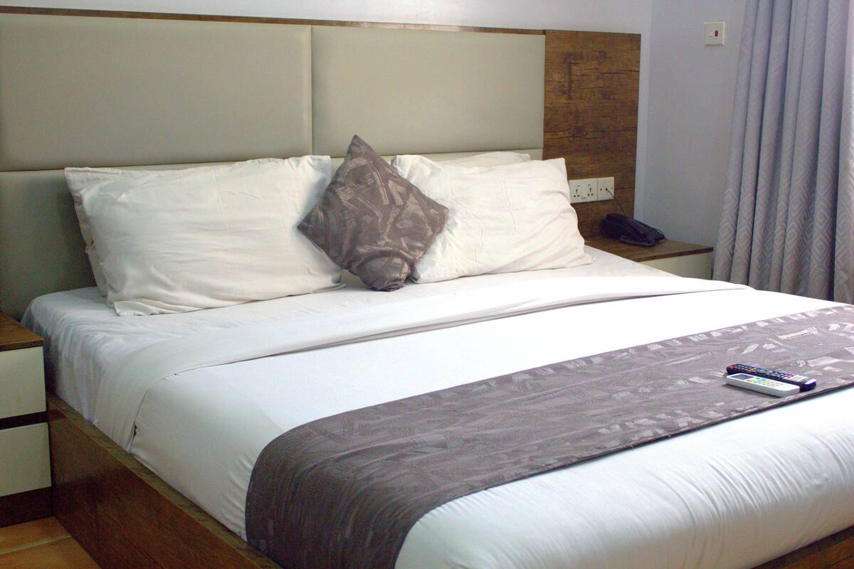 Una cama bien tendida con sábanas blancas, un plaid gris y un control remoto sobre la cama.