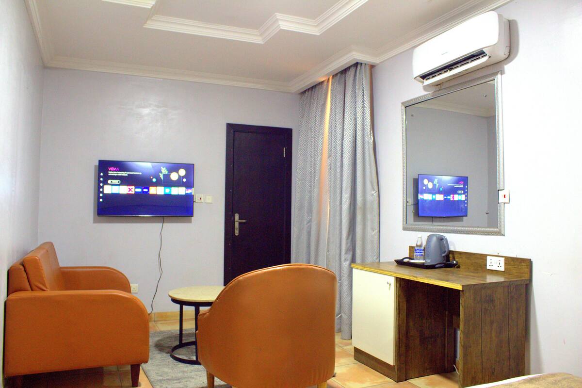 Habitación de hotel con televisión montada en la pared, escritorio con cafetera y dos sillones anaranjados.
