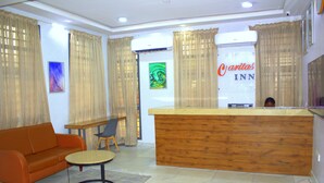 A hotel lobby with a reception desk, a sofa, a small table, and a chair. - Caritas Inn Ilasan (Lekki)