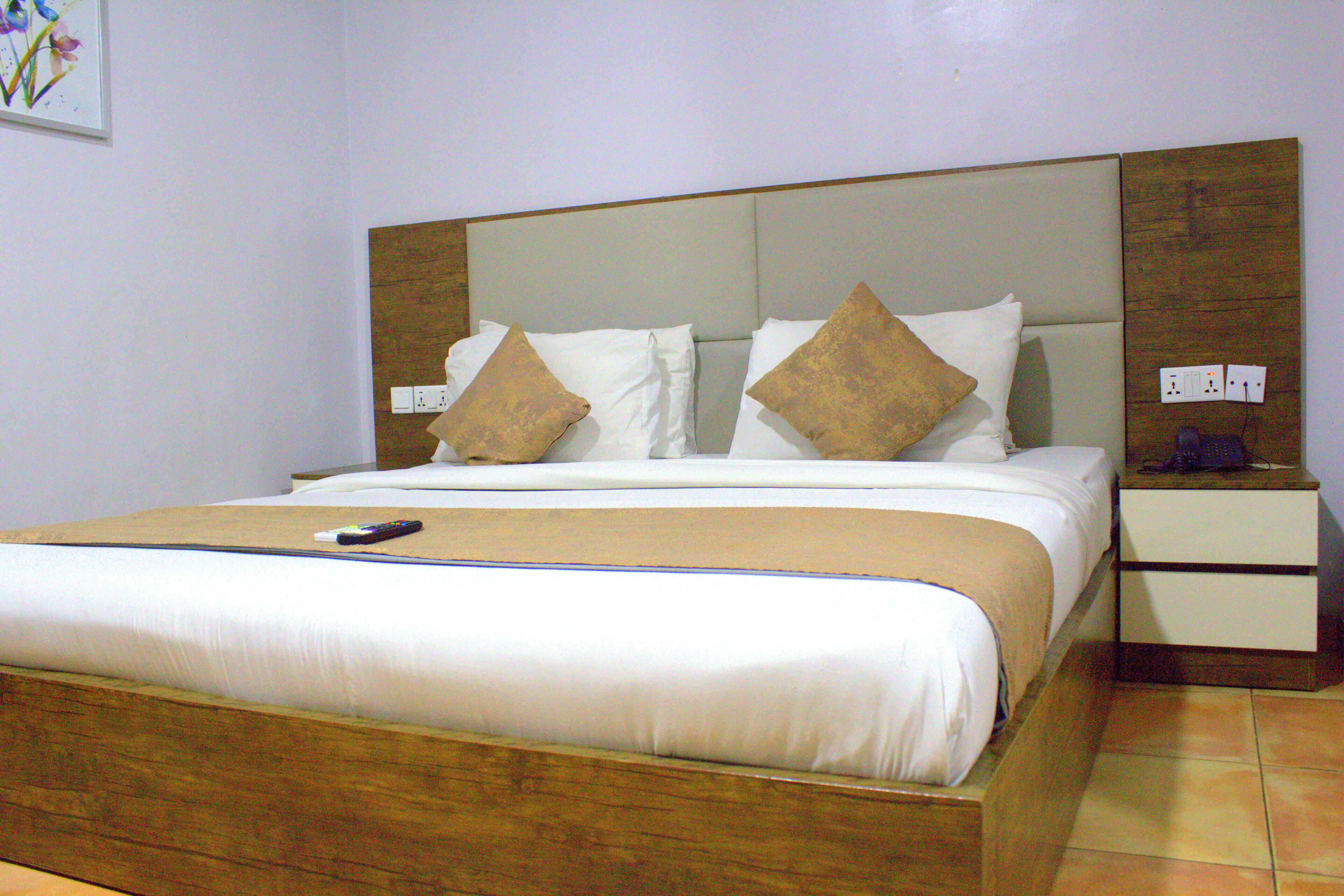Une chambre d’hôtel avec un grand lit, une tête de lit en bois, une table de chevet avec une lampe et un tableau au mur.