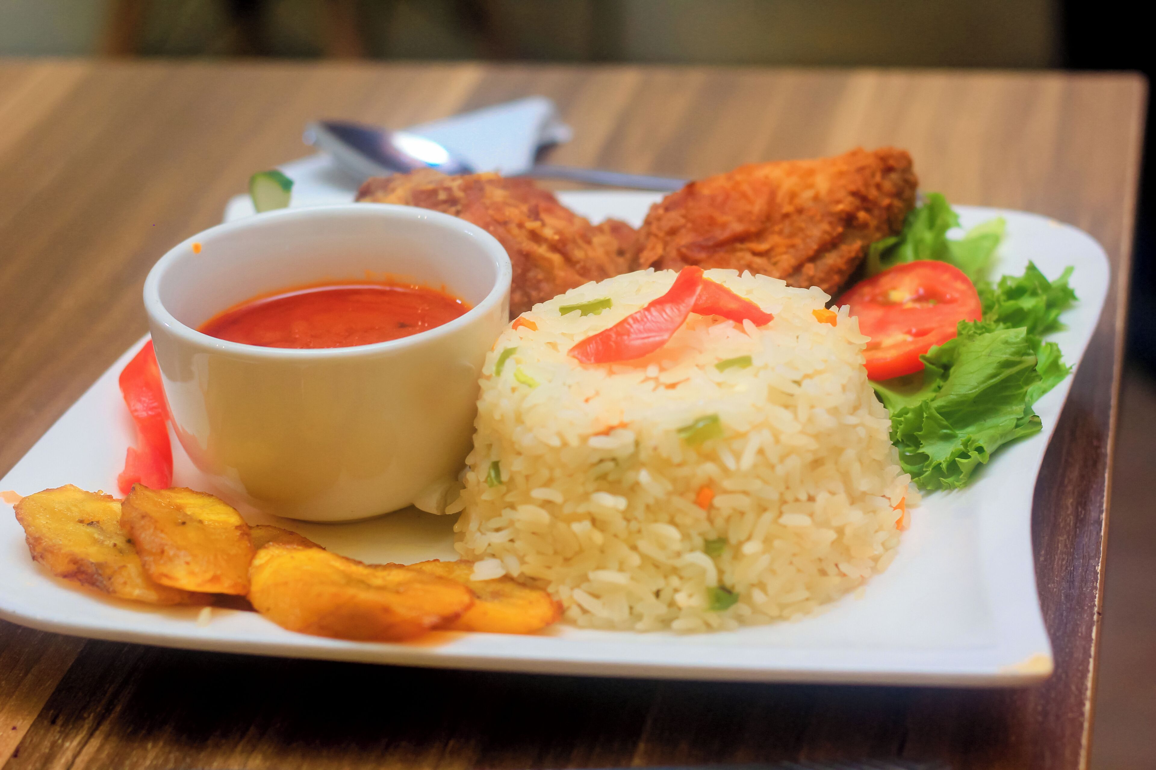 A plate of food with rice, fried chicken, and a small bowl of sauce.