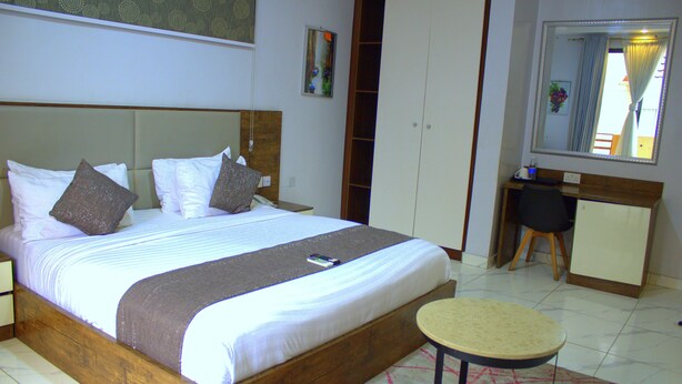 A neatly made bed with a wooden headboard, a bedside table, a small round table, and a wardrobe. - Caritas Inn Ilasan (Lekki)