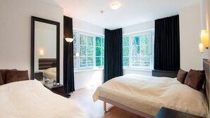 Une chambre d’hôtel avec deux lits, une grande fenêtre, un miroir et une table de chevet avec une lampe.