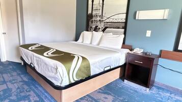 Quarto de hotel com cama, mesa de cabeceira, telefone e luminária fixada na parede.